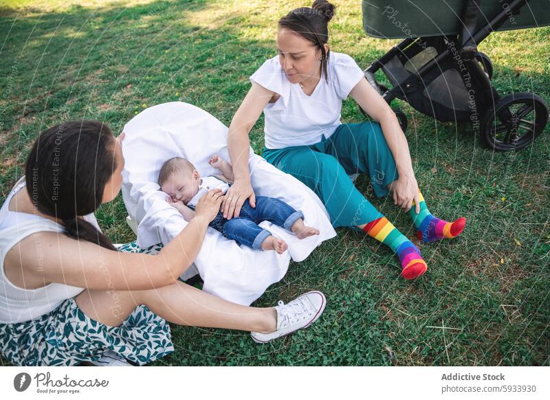 Lesbian couple caring for baby in stroller at the park mother lesbian lgbt grass outdoor colombian bonding love care family rest sleeping parenting nurture