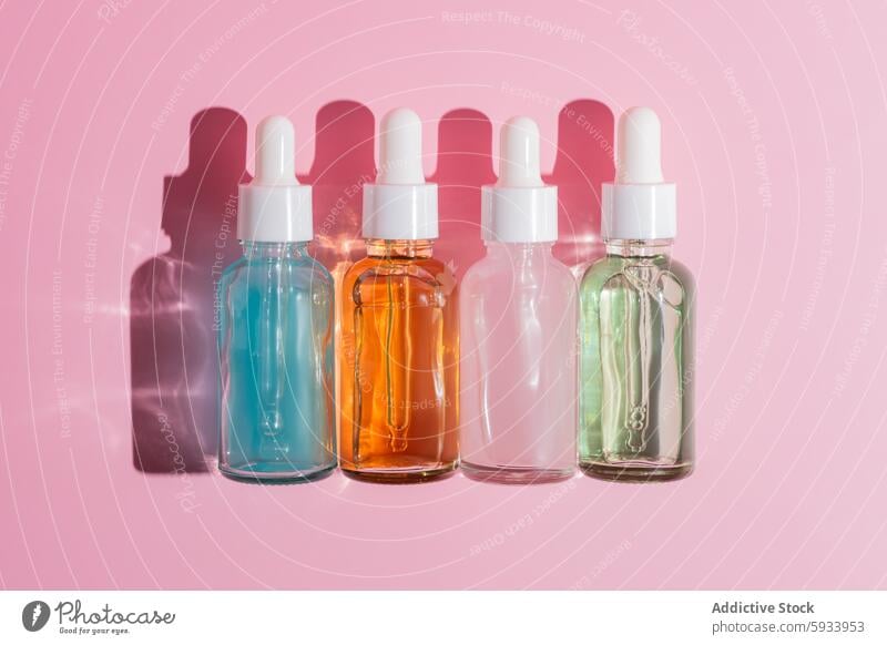 Colorful serum dropper bottles against pink background top view skincare beauty product pastel shadow colorful liquid cosmetic glass container alignment health