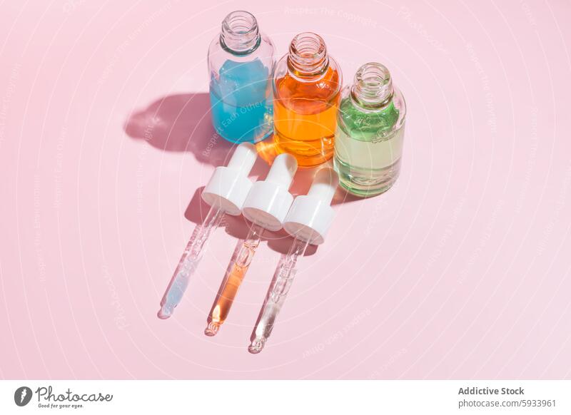 Colorful Serum Bottles with Droppers on Pink Background serum dropper bottle pink background translucent liquid blue orange green shadow beauty skincare