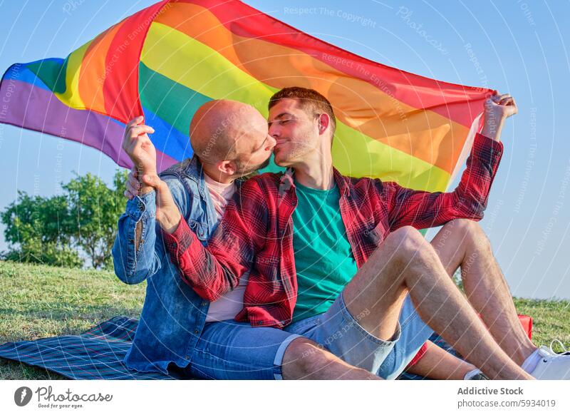 Gay couple expressing love under a pride flag outdoors gay kiss man affection relationship support rainbow emotion romantic diverse summer park cheerful adult