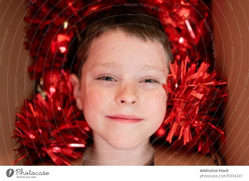 Young boy surrounded by festive red Christmas decorations christmas tinsel ornament happy joy holiday spirit child cheerful smile seasonal winter celebration