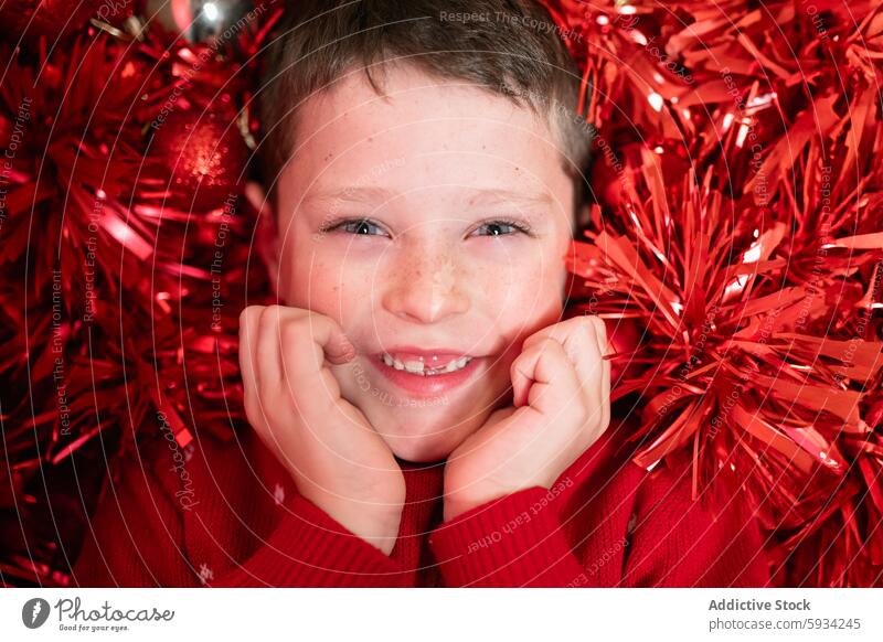 Delightful young boy enjoying Christmas decorations christmas red tinsel ornament smile holiday festive cheerful excitement seasonal happy child spirited fun