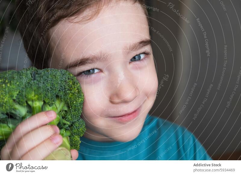 Young boy with a vibrant smile holding fresh broccoli child healthy eating cheerful fun vegetable green nutrition diet playful eyes face half-hidden happiness