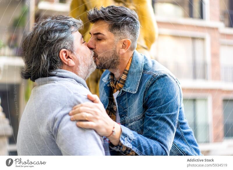 Gay couple kissing passionately outdoors gay mature men love affection street city romantic tenderness relationship denim jacket grey hair embrace homosexual