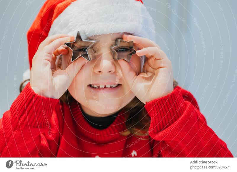 Festive girl playing with cookie cutters twin christmas festive santa hat red sweater joy holiday cooking baking child celebration winter december cheerful