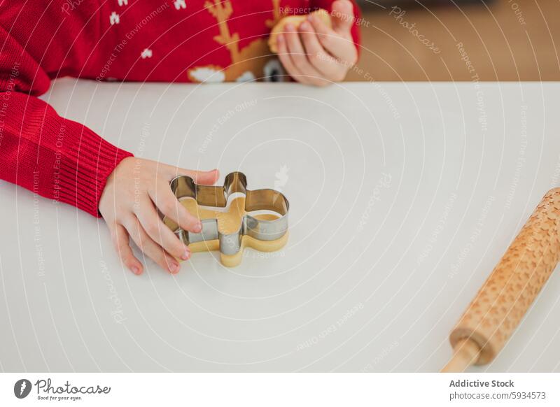 A child baking Christmas cookies in festive attire cooking christmas holiday sweater red dough cutter snowflake joy spirit seasonal kitchen rolling pin