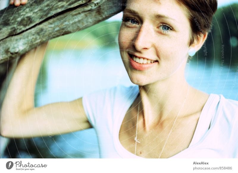 A slim, young woman stands on the shore of the bathing lake leaning against a tree Young woman Youth (Young adults) Face Freckles 18 - 30 years Adults Branch