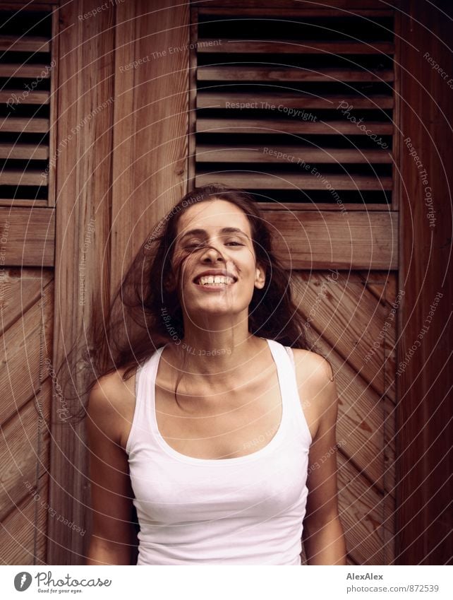 Young woman in front of a wooden door waves her long hair laughing Youth (Young adults) 18 - 30 years Adults Undershirt Black-haired Long-haired Wooden door