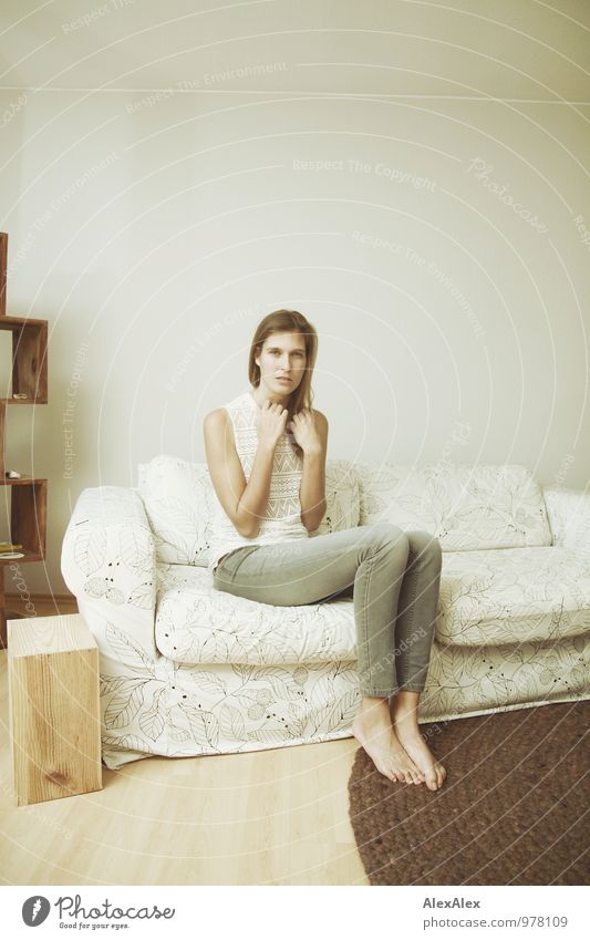 young tall woman sits on a light couch Flat (apartment) Furniture Sofa Young woman Youth (Young adults) Body Barefoot 18 - 30 years Adults Jeans Top Brunette